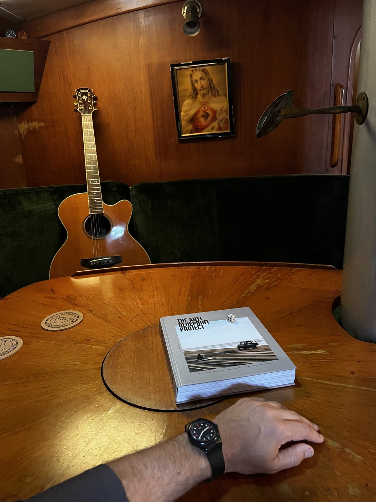 The saloon table aboard Library - a guitar, a book, framed art and an anchor on the teak