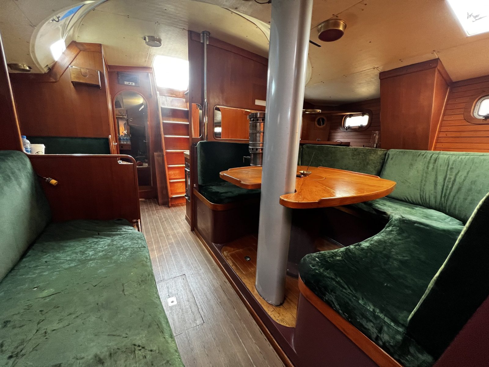 The saloon looking aft - green settees and a teak table around the mast post